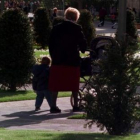 Una anciana pasea con sus nietos, uno de la mano y otro en un cochecito.