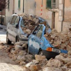 Una mujer contempla los destrozos provocados por el terremoto en dos vehículos en L´Aquila