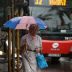 Una mujer camina bajo la lluvia con gabardina y paraguas.