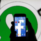 Dos hombres observan un smartphone con el logo de Facebook delante de una imagen del logo de Whatsapp.