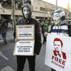 Dos manifestantes con máscaras de Anonymous sujetan pancartas de apoyo a Julian Assange.