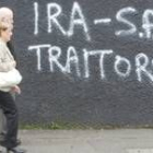 Una pareja pasa en Belfast ante un muro en el que se lee «IRA y Sinn Fein, traidores»