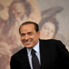 Berlusconi sonríe mientras toma asiento en una rueda de prensa en Roma.