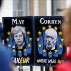 Unos peatones pasan junto a carteles con la primera ministra británica, Theresa May, y el líder del Partido Laborista, Jeremy Corbyn, cerca del Parlamento, en Londres.