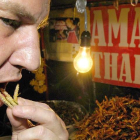 Un hombre prueba gusanos fritos en un puesto de comida en Bangkok.