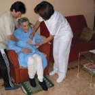 Una sanitaria y una familiar ayudan a incorporarse a una anciana aquejada de alzhéimer