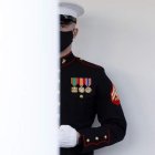 Un marine custodia la puerta principal de la Casa Blanca horas antes de la llegada del nuevo presidente, Joe Biden. Miles de banderas jalonan la avenida que lleva al Capitolio la víspera de la toma de psosesión de Biden. Jacob Anthony Chansley durante el asalto a la Cámara de Representantes. En la otra página, tropas con trajes de época marchan en el ensayo del traspaso de poderes