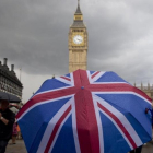 Un transeúnte se refugia de la lluvia en un paraguas con la bandera británica, cerca del Big Ben.