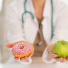 Una doctora dando a elegir entre un donut o una manzana.