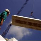 Un obrero supervisa la labor de carga de una grúa que coloca una plancha en el tejado de un edificio