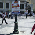 Varios viandantes pasan junto a un cartel del sindicato asociado al partido comunista PAME que anuncia la convocatoria de una manifestación por el Día Internacional del Trabajo, en Atenas.