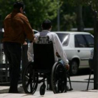 Un discapacitado es ayudado por su cuidador para desplazarse con su silla de ruedas