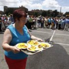 Una mujer lleva varios platos de paella durante la jornada de convivencia vecinal en León.