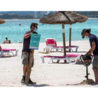 Dos operarios ponen a punto las sombrillas de la playa balear de Alcudia, en Mallorca. CATI CLADERA