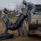 Autoridades forenses recogen cadáveres envueltos en plásticos para su traslado a la morgue, hoy, en Bucha (Ucrania). MIGUEL GUTIÉRREZ