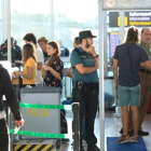 Un usuario pasa bajo el arco de detección de metales de la T-1 del aeropuerto de El Prat ante la mirada de dos guardias civiles