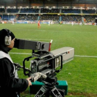 Un cámara de una cadena de televisión toma imágenes durante un partido de fútbol.