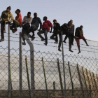 Policías españoles tratan de disuadir a inmigrantes encaramados a la valla de Melilla, fronteriza con Marruecos.