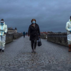 Una viandante cruza el Puente Romano de Ourense mientras empleados municipales lo desinfectan este martes. BRAIS LORENZO