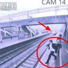 Momento en el que la mujer, detrás del hombre, le agarra del brazo y evita que se tire a la vía de tren.