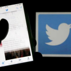 Un usuario de Twitter lee mensajes de esta red social en el móvil frente al logo del pájaro, símbolo de la misma.