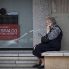 Una mujer mayor habla por teléfono móvil al lado de un cartel de planes de pensiones.