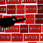 Sombra de un hombre sujetando un mando a distancia sobre el fondo del logo de Netflix.