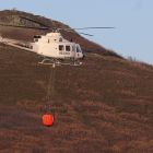 Un helicóptero se retira del incendio antes del anochecer, cerca de Bouzas.