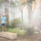 Varias personas se refrescan bajo unos surtidores de agua vaporizada en el centro de Valencia. BIEL ALIÑO