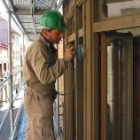 Un alumno de carpintería pule el exterior de la balconada de la casa solariega