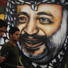 Dos palestinos pasean frente a un mural del expresidente palestino Arafat.