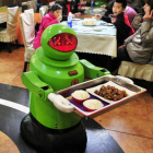 El androide sirve la comida ante la atenta mirada de unos niños.