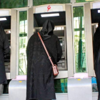 Tres mujeres ataviadas con velo negro sacan dinero de un cajero en Irán.