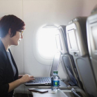 Una usuaria navega por internet a través de wifi en un avión con su portátil.