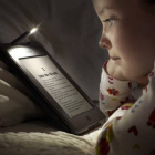 Imagen de archivo de una niña leyendo en la cama un libro electrónico.