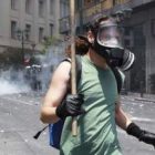 Un manifestante con una máscara de gas huye del lugar donde se concentran los antidisturbios.