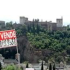Un cartel anunciando la venta de una propiedad se recorta sobre la Alhambra de Granada