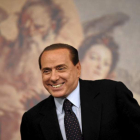 Silvio Berlusconi sonríe mientras toma asiento en una rueda de prensa.