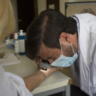 El dermatólogo José Castiñeiras González observa con una lupa la lesión en la piel para confirmar la sarna. FERNANDO OTERO