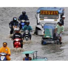 Filipinos conducen hoy por una calle inundada del suburbio de Paranaque, al sur de Manila.