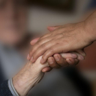 Un cuidador coge la mano de un enfermo de alzhéimer.