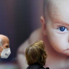 Dos personas con mascarilla pasan por delante de un cartel con la imagen de un bebé.  DAL ZENNARO
