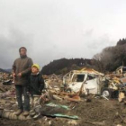 Una familia camina bajo la lluvia entre los escombros en la ciudad costera de Rikuzentakata.