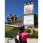 Un peregrino se detiene ante el castillo, con el cartel anunciando la exposición.