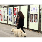 Una mujer pasea tranquilamente con su perro ante los carteles electorales, en Bilbao.