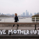 Una mujer cruza el puente de Waterloo donde se puede leer el mensaje «salva a la madre Tierra» en Londres. WILL OLIVER