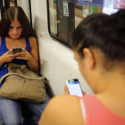 Dos chicas consultan en el metro sus respectivos móviles.