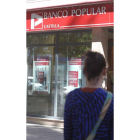 La joven Laura, de espaldas, ante la sucursal bancaria.