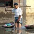 Un hombre chino porta una balanza mientras atraviesa un río