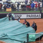 Operarios cubren con una lona la pista en la que disputaban su partido Torró y Zakopalova.